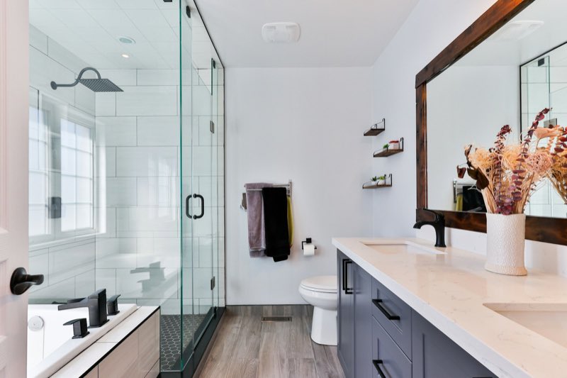 Bright bathroom with a glass shower, wooden floor and dried flowers